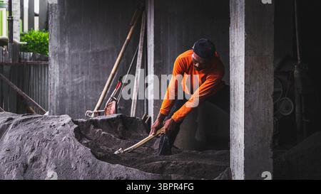 Ein Bauarbeiter, der Sand vor Ort manuell hackt, zeigt Entschlossenheit, körperliche Arbeit und Beharrlichkeit bei der Vorbereitung der Bodenarbeiten. Stockfoto