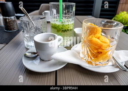 Tasse Kaffee, Gurkenlimonade und Aprikoseneis im Glas auf dem Restauranttisch. Stockfoto