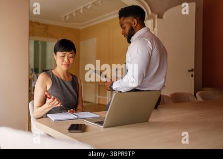 Geschäftsmann, der ein digitales Tablet verwendet und Ideen erklärt, während die Frau Notizen macht und im Büro zusammenarbeitet Stockfoto