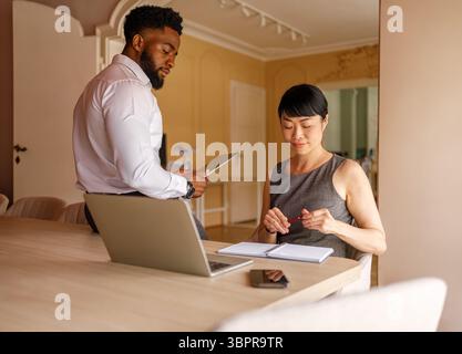 Männlicher Unternehmer, der ein digitales Tablet verwendet und Strategien diskutiert, während Geschäftsfrau sich Notizen am Schreibtisch im Büro macht Stockfoto