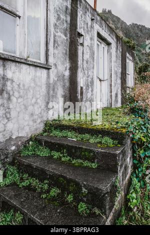 Verlassene Steintreppen Mit Moosbewuchs Führen Zum Verwitterten Gebäude In Sao Jorge Azoren. Bewachsene Vegetation, verfallene Fassade, ländlicher Verfall, Hafen Stockfoto