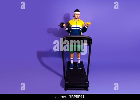 Junger Mann, der Fitness und Genuß auf dem Laufband mit lebendigem Hintergrund und kontrastierenden Requisiten ausbalanciert Stockfoto
