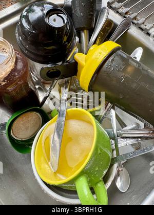 Überfüllte Küchenspüle gefüllt mit schmutzigem Geschirr, Tassen und Besteck nach einer Mahlzeit zu Hause. Stockfoto