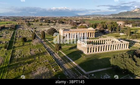 Blick aus der Vogelperspektive auf die antiken Ruinen von Paestum mit zwei großen Tempeln, umgeben von grünen Feldern und archäologischen Stätten. Die Landschaft umfasst Bäume Stockfoto