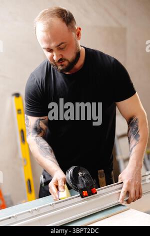 Builder preparing aluminum profiles for stretch ceiling using special equipment in apartment being renovated Stockfoto