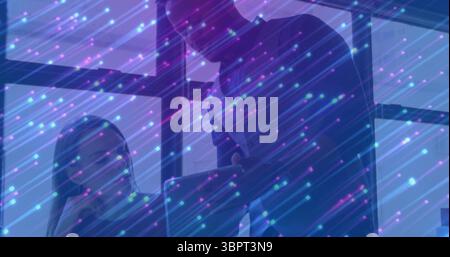 Kollegen, die in Geschäftskleidung zusammenarbeiten, neigen sich am Bürotisch zu einem Notebook, mit Datenüberlagerung Stockfoto