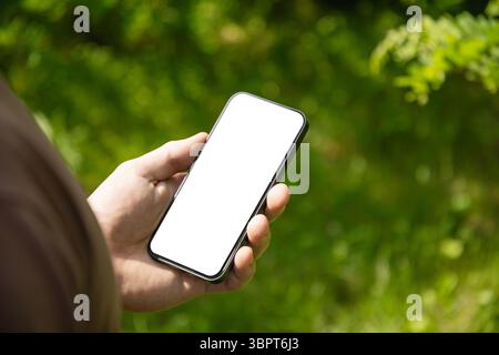 Mans Hände halten Smartphone mit weißem, leerem Bildschirm in grüner Außeneinstellung. Überprüfen Sie Apps, die sich auf Geräte, Chats und SMS konzentrieren. Fitnessfortschritt ein Stockfoto