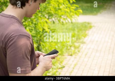 Nahaufnahme der Hände des Mannes, die das Smartphone im grünen Außenbereich halten. Überprüfen Sie Apps, die sich auf Geräte, Chats und SMS konzentrieren. Fitnessfortschritt auf App. Seite VI Stockfoto