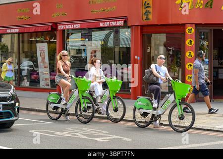 London, England, Großbritannien - 4. Juli 2025: Gruppe von Personen, die Lime-Fahrräder auf einer Straße im Zentrum von London mieten Stockfoto