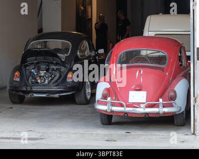 Zwei VW-Käfer in einer Werkstatt. Der schwarze mit offener Motorhaube, der rote mit Patina – beide wahrscheinlich geliebte Oldtimer. Stockfoto