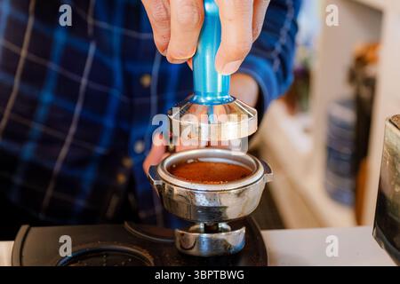 Der Barista verwendet einen blauen Metalltamper, um gemahlenen Kaffee in Portafilter zu verdichten, ein wesentlicher Schritt für die Zubereitung eines perfekten Espresso. Stockfoto