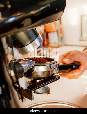 Nahaufnahme eines Barista, der mit einer professionellen Espressomaschine frischen Kaffee in einen Portafilter mahlt. Das Bild erfasst handwerkliches Können und Qualität in Stockfoto