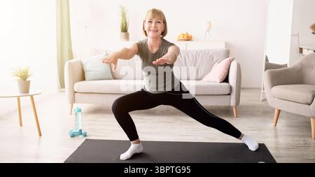 Glückliche ältere Dame, die Ausfallschritte beim häuslichen Training im Wohnzimmer macht, Platz kopieren Stockfoto