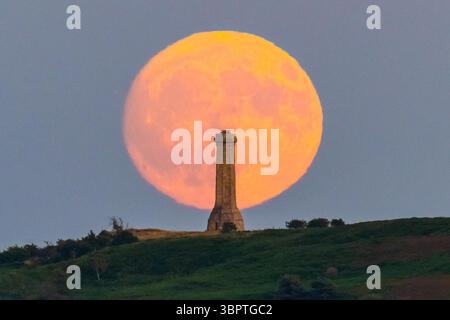 Portesham, Dorset, Großbritannien. Juli 2025. Wetter in Großbritannien. Der fast volle Buck-Mond erhebt sich hinter dem Hardy Monument in der Nähe von Portesham in Dorset in den klaren Abendhimmel. Das Denkmal in Form eines Teleskops wurde 1844 in Gedenken an Vizeadmiral Sir Thomas Masterman Hardy errichtet, der Flaggenkapitän der HMS Victory in der Schlacht von Trafalgar war. Bildnachweis: Graham Hunt/Alamy Live News. Bildnachweis: Graham Hunt/Alamy Live News Stockfoto