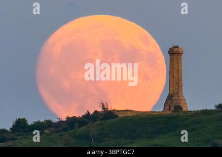 Portesham, Dorset, Großbritannien. Juli 2025. Wetter in Großbritannien. Der fast volle Buck-Mond erhebt sich hinter dem Hardy Monument in der Nähe von Portesham in Dorset in den klaren Abendhimmel. Das Denkmal in Form eines Teleskops wurde 1844 in Gedenken an Vizeadmiral Sir Thomas Masterman Hardy errichtet, der Flaggenkapitän der HMS Victory in der Schlacht von Trafalgar war. Bildnachweis: Graham Hunt/Alamy Live News. Bildnachweis: Graham Hunt/Alamy Live News Stockfoto