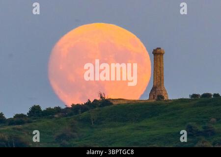 Portesham, Dorset, Großbritannien. Juli 2025. Wetter in Großbritannien. Der fast volle Buck-Mond erhebt sich hinter dem Hardy Monument in der Nähe von Portesham in Dorset in den klaren Abendhimmel. Das Denkmal in Form eines Teleskops wurde 1844 in Gedenken an Vizeadmiral Sir Thomas Masterman Hardy errichtet, der Flaggenkapitän der HMS Victory in der Schlacht von Trafalgar war. Bildnachweis: Graham Hunt/Alamy Live News. Bildnachweis: Graham Hunt/Alamy Live News Stockfoto