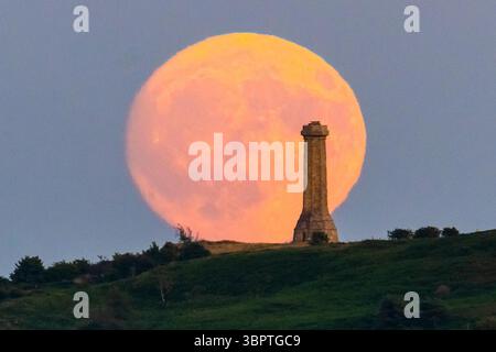 Portesham, Dorset, Großbritannien. Juli 2025. Wetter in Großbritannien. Der fast volle Buck-Mond erhebt sich hinter dem Hardy Monument in der Nähe von Portesham in Dorset in den klaren Abendhimmel. Das Denkmal in Form eines Teleskops wurde 1844 in Gedenken an Vizeadmiral Sir Thomas Masterman Hardy errichtet, der Flaggenkapitän der HMS Victory in der Schlacht von Trafalgar war. Bildnachweis: Graham Hunt/Alamy Live News. Bildnachweis: Graham Hunt/Alamy Live News Stockfoto