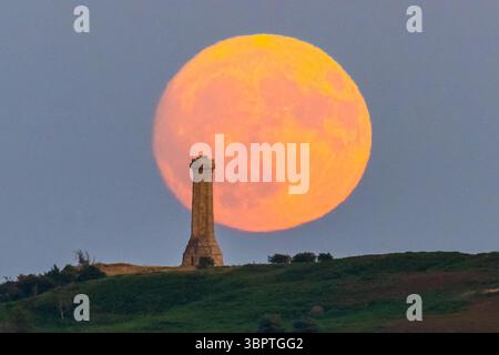 Portesham, Dorset, Großbritannien. Juli 2025. Wetter in Großbritannien. Der fast volle Buck-Mond erhebt sich hinter dem Hardy Monument in der Nähe von Portesham in Dorset in den klaren Abendhimmel. Das Denkmal in Form eines Teleskops wurde 1844 in Gedenken an Vizeadmiral Sir Thomas Masterman Hardy errichtet, der Flaggenkapitän der HMS Victory in der Schlacht von Trafalgar war. Bildnachweis: Graham Hunt/Alamy Live News. Bildnachweis: Graham Hunt/Alamy Live News Stockfoto