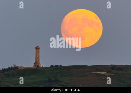 Portesham, Dorset, Großbritannien. Juli 2025. Wetter in Großbritannien. Der fast volle Buck-Mond erhebt sich hinter dem Hardy Monument in der Nähe von Portesham in Dorset in den klaren Abendhimmel. Das Denkmal in Form eines Teleskops wurde 1844 in Gedenken an Vizeadmiral Sir Thomas Masterman Hardy errichtet, der Flaggenkapitän der HMS Victory in der Schlacht von Trafalgar war. Bildnachweis: Graham Hunt/Alamy Live News. Bildnachweis: Graham Hunt/Alamy Live News Stockfoto