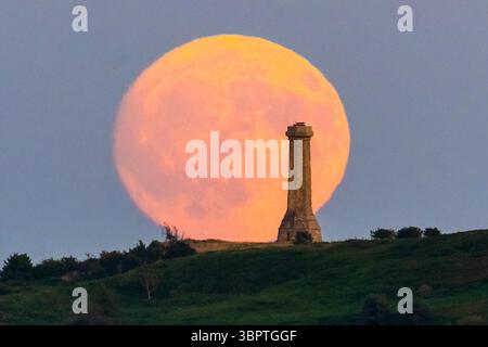 Portesham, Dorset, Großbritannien. Juli 2025. Wetter in Großbritannien. Der fast volle Buck-Mond erhebt sich hinter dem Hardy Monument in der Nähe von Portesham in Dorset in den klaren Abendhimmel. Das Denkmal in Form eines Teleskops wurde 1844 in Gedenken an Vizeadmiral Sir Thomas Masterman Hardy errichtet, der Flaggenkapitän der HMS Victory in der Schlacht von Trafalgar war. Bildnachweis: Graham Hunt/Alamy Live News. Bildnachweis: Graham Hunt/Alamy Live News Stockfoto