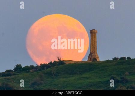 Portesham, Dorset, Großbritannien. Juli 2025. Wetter in Großbritannien. Der fast volle Buck-Mond erhebt sich hinter dem Hardy Monument in der Nähe von Portesham in Dorset in den klaren Abendhimmel. Das Denkmal in Form eines Teleskops wurde 1844 in Gedenken an Vizeadmiral Sir Thomas Masterman Hardy errichtet, der Flaggenkapitän der HMS Victory in der Schlacht von Trafalgar war. Bildnachweis: Graham Hunt/Alamy Live News. Bildnachweis: Graham Hunt/Alamy Live News Stockfoto