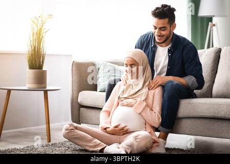Fürsorglicher arabischer Ehemann, der Schultermassage für schwangere muslimische Frau macht Zu Hause Stockfoto