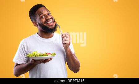 Fröhlicher Schwarzer Kerl Essen Salat Genießen Gesunde Mahlzeit, Gelber Hintergrund Stockfoto
