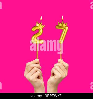 Geburtstag auf Fuchsiahintergrund mit der Zahl 27 - Hände mit Zahlenkerzen Stockfoto