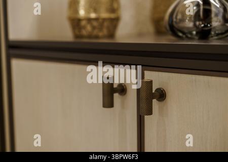 Makrodetail von zwei modernen Schrankgriffen mit T-Steg mit gerändelter Bronze, montiert auf hellen Holztüren. Hochwertige Möbelbeschläge. Stockfoto