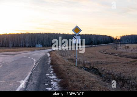 Kreuzung auf einer Landstraße im Herbst bei Sonnenuntergang. Straßenschild einer Abzweigung außerhalb der Stadt. Stockfoto