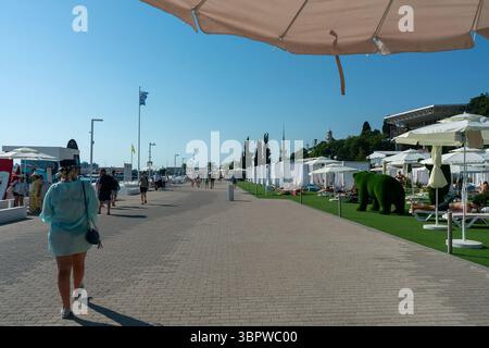 Sotschi, Russland - 5. Juli 2022: Eine Gasse am Meer mit Sonnenschirmen und Bungalows. Urlauber schlendern entlang des Ufers des Kurorts. Stockfoto