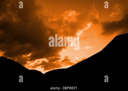 Silhouetten-Bergrücken erstrecken sich über flache Vektoren mit orangefarbenem Himmel und Wolken Stockfoto
