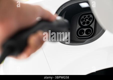 Nahaufnahme des Ladeanschlusses und des Steckers des Elektrofahrzeugs, der mit der Hand verbunden werden soll Stockfoto