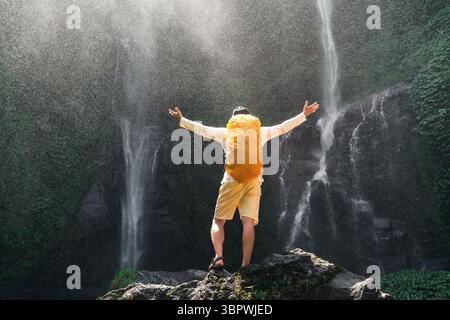 Ein Rucksackreisender steht mit erhobenen Armen vor Sekumpul, dem höchsten Wasserfall in Bali, Indonesien Stockfoto