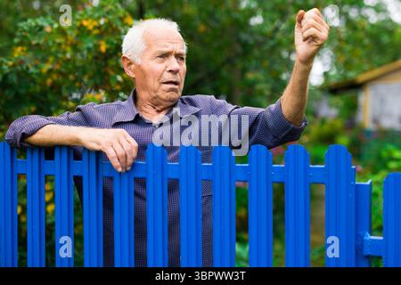 Alter Mann zeigt Faust im Freien neben dem Zaun Stockfoto