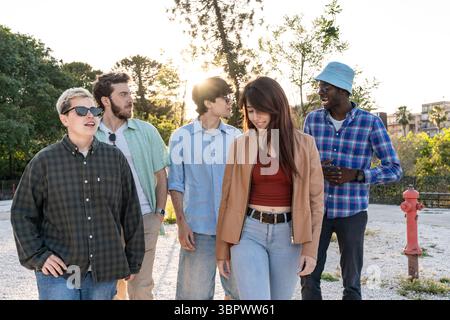 Eine abwechslungsreiche Gruppe fröhlicher junger Freunde, die Seite an Seite laufen und sich in einem wunderschönen warmen Park entspannt unterhalten Stockfoto