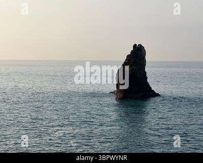 Eine dramatische Felsformation erhebt sich bei Sonnenuntergang aus dem ruhigen Meer. Stockfoto