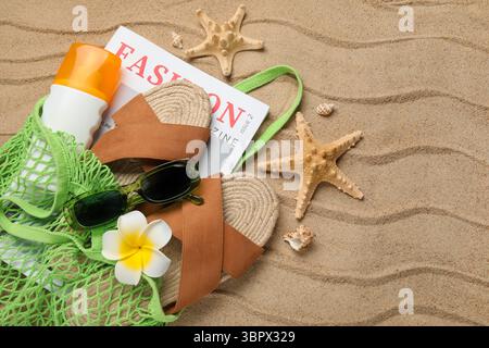Schnur-Tasche mit Flasche Sonnencreme, Magazin und Strandaccessoires auf Sand als Hintergrund, Nahaufnahme Stockfoto