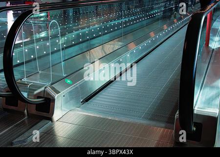 Fast leere Laufstege in einem internationalen Flughafenkorridor. Reflexion von wenigen Menschen, die Koffer schleppen. Futuristisches Design von Glasgeländern. Stockfoto