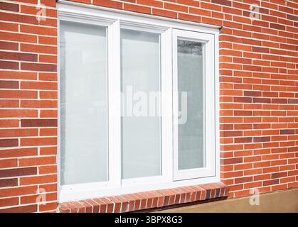 PVC-Fenster an der Fassade eines Privathauses. Ein echter moderner Fensterrahmen in einem neuen Backsteinhaus. Neu installierte, doppelt verglaste UPVC-Fenster in einer h Stockfoto