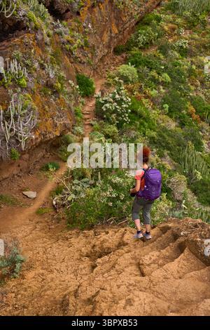 Weibliche Wanderer, die steile vulkanische Pfade durch trockenes und üppiges Gelände in Anaga, Teneriffa, absteigen Stockfoto