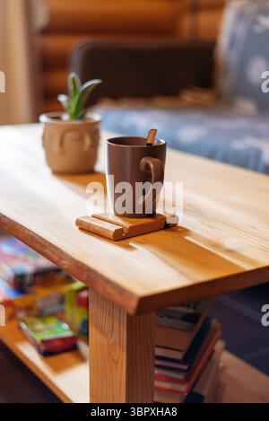 Eine gemütliche Wohnzimmerszene mit einem hölzernen Couchtisch mit einem Becher und einer kleinen Pflanze. Bücher und Spiele werden im unteren Regal aufbewahrt, und eine Couch ist V Stockfoto