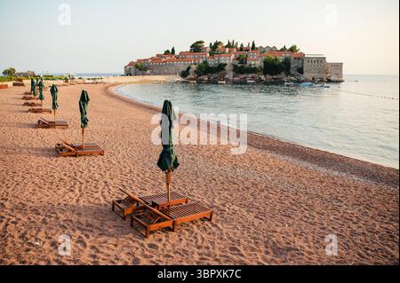 Leerer Strand mit Holzliegen und geschlossenen Sonnenschirmen mit Blick auf eine historische Inselstadt. Stockfoto