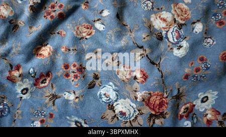 Fotohintergrund aus bedrucktem Stoff. Chaotische Falten. Verzierung verschiedener Blumen und Blätter. Weiß, pfirsichfarben, rot und schwarz. Blauer Hintergrund. Stockfoto