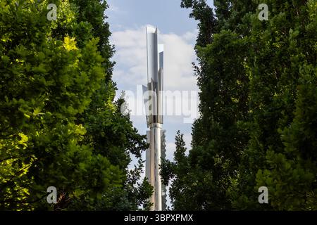 Posen, Polen - 18. Juni 2025: Moderne Stela Heinza Macka-Skulptur aus Metall mit geometrischen Formen, die von üppigen grünen Bäumen eingerahmt werden und eine zeitgenössische Kneipe zeigen Stockfoto