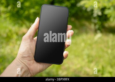 Nahaufnahme von Frauenhänden, die das Smartphone in grüner Umgebung halten. Überprüfen Sie Apps, die sich auf Geräte, Chats und Leistungsdaten konzentrieren. Sprachassistent. Fitn Stockfoto