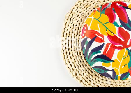 Ansicht von oben auf braune Korbplatte, bunte Platte auf weißem Hintergrund. Rundes Tablett mit Strohhalm, exotischer Pflanzenteller, Sommer-Picknick. Flache Ladefläche, Kopierraum. Stockfoto