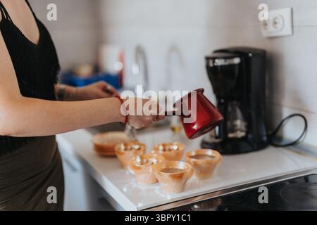In der Mitte der Frau in der Küche, die heissen Kaffee in kleine Tassen mit einer traditionellen türkischen Kanne gießt Stockfoto