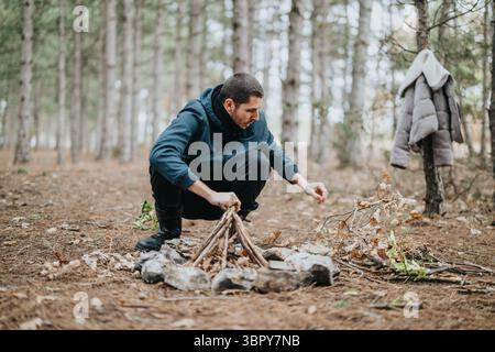 Mann, der ein Lagerfeuer in einem bewaldeten Bereich während einer ungezwungenen Outdoor-Aktivität vorbereitet Stockfoto