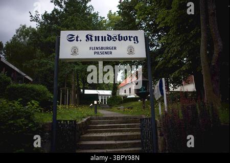Flensburg, Schleswig-Holstein das Foto zeigt den Eingang zur St. Knudsborg im Flensburger Stadtteil Sandberg, nahe dem Bahnhof. Im Vordergrund führt eine Steintreppe durch einen kleinen Garten hinauf zu einem weißen Schild mit der Aufschrift St. Knudsborg Flensburger Pilsener. Der Weg ist von Bäumen und Sträuchern gesäumt, im Hintergrund sind ein historisches Gebäude mit rotem Dach sowie weitere Anbauten zu erkennen. Die Atmosphäre wirkt ruhig und einladend, typisch für ein traditionsreiches Haus in einer grünen Umgebung. Aufnahme vom 10.07.2025, Flensburg, Sandberg *** Flensburg, Schleswig Ho Stockfoto